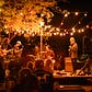 A four person band plays outdoors under a canopy of string lights at night.